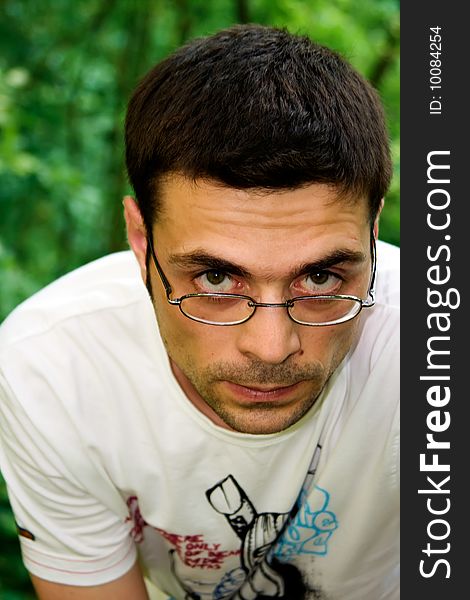 Portrait of young male in glasses and white t-shirt looking seriously, in the forest. Portrait of young male in glasses and white t-shirt looking seriously, in the forest