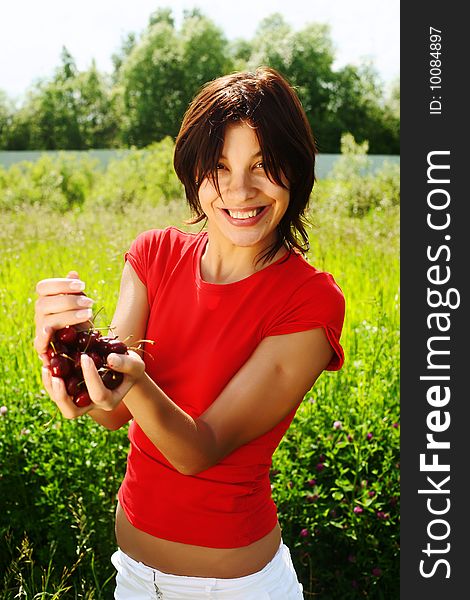 Young beautiful girl with cherries in their hands against a background of grass