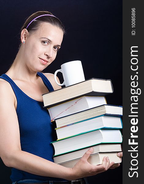 A young woman carrying a load of heavy books and coffee on a dark background. A young woman carrying a load of heavy books and coffee on a dark background.