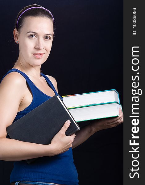 A young woman with books on a dark background. A young woman with books on a dark background.