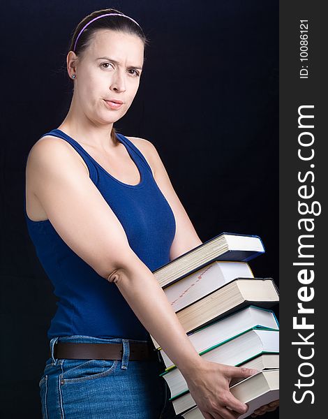 A young woman carrying a load of heavy books on a dark background. A young woman carrying a load of heavy books on a dark background.