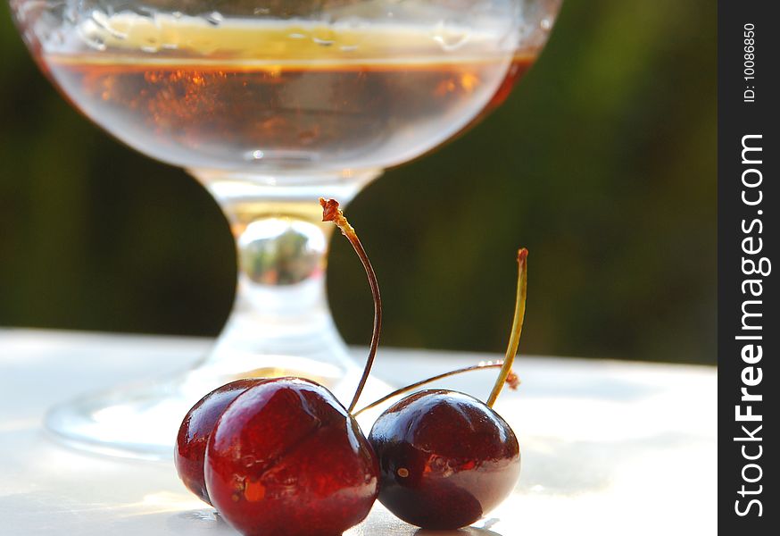 Three cherries in front of a glass of cognac with a shallow depht of field. Three cherries in front of a glass of cognac with a shallow depht of field