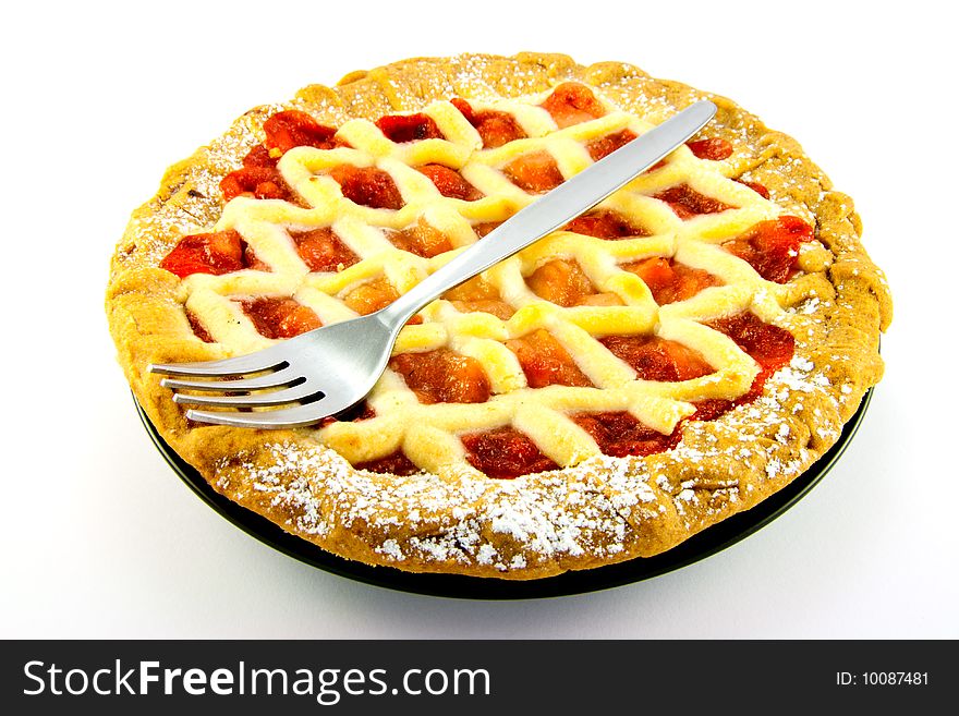 Whole apple and strawberry pie on a black plate with a fork on a white background. Whole apple and strawberry pie on a black plate with a fork on a white background