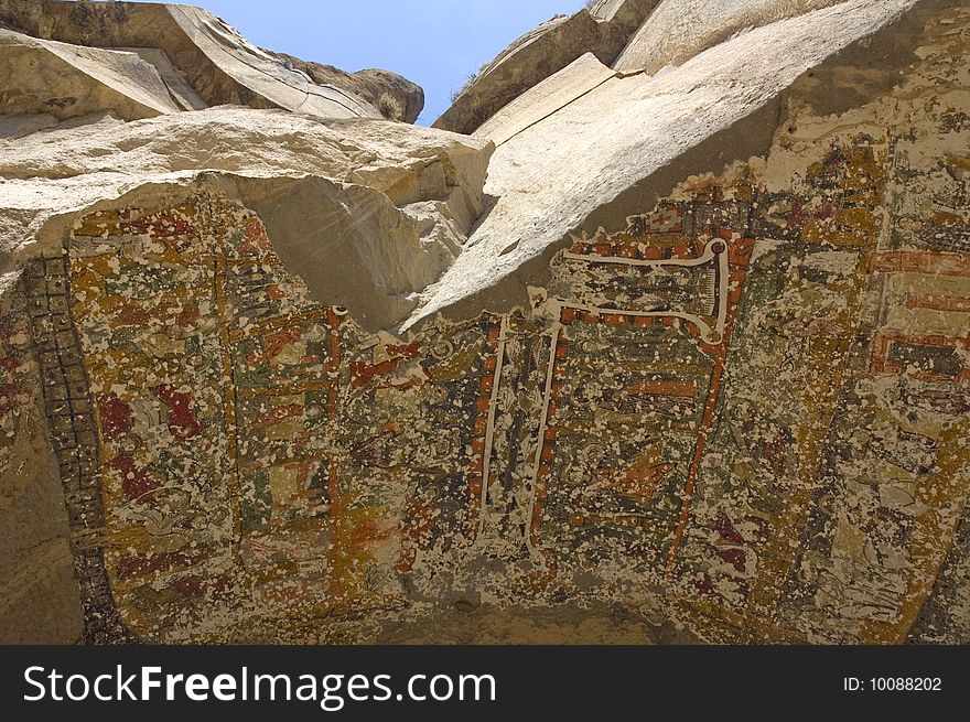 A chapel ceiling painted on the underside of rocks in Ilhara Canyon.  Early Christian painting of elaborate cross and biblical scenes.  Rock has eroded, leaving fractured artwork on the ceiling of the chapel.  View looking up of canyon rocks.  Blue sky. A chapel ceiling painted on the underside of rocks in Ilhara Canyon.  Early Christian painting of elaborate cross and biblical scenes.  Rock has eroded, leaving fractured artwork on the ceiling of the chapel.  View looking up of canyon rocks.  Blue sky.