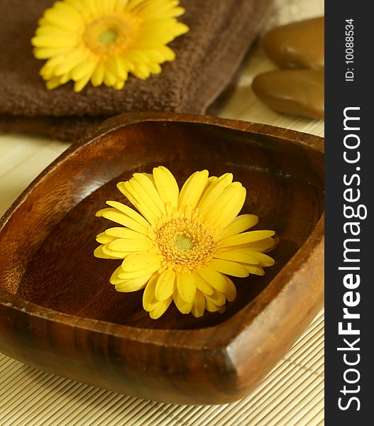Yellow flower floating in wooden bow, towel and stones. spa background