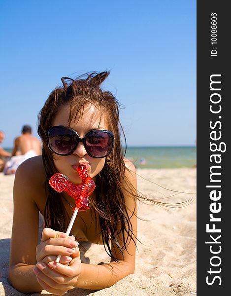 Girl in sunglasses with candy at the sea on the sand