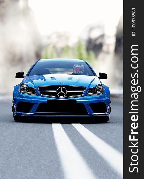Front of blue Mercedes Benz large luxury saloon approaching along two white road markings, blurred background. Front of blue Mercedes Benz large luxury saloon approaching along two white road markings, blurred background.