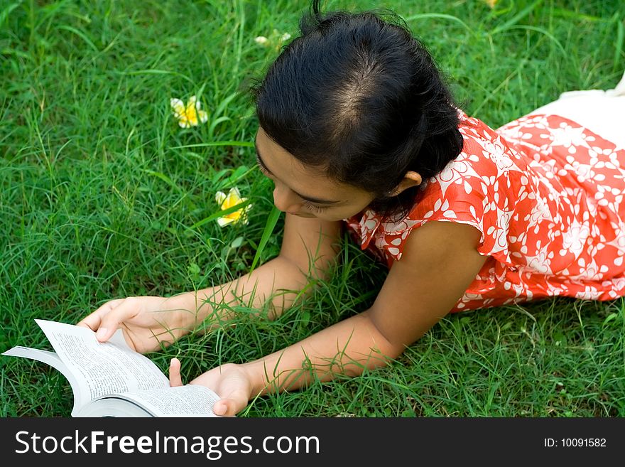 Lifestyle portrait of asian woman laying down on the green grass seems to enjoy her leisure time, reading her favorite novel. Lifestyle portrait of asian woman laying down on the green grass seems to enjoy her leisure time, reading her favorite novel