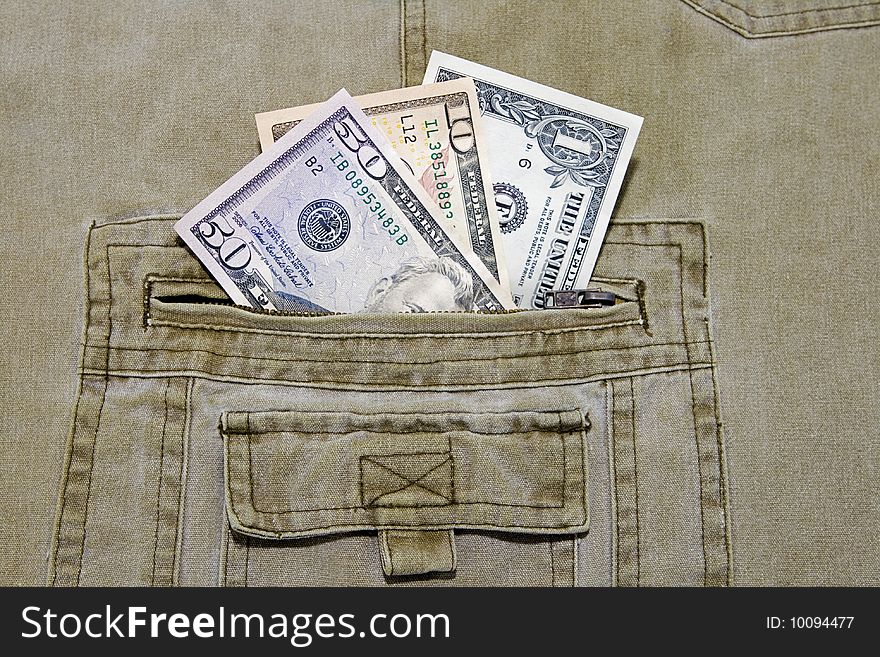 Three different US currency dollar notes in the pocket of a pair of khaki trousers