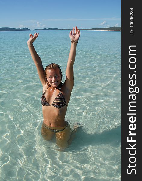 Beautiful young teenage girl standing in water at paradise beach with turquoise water raising hands above head