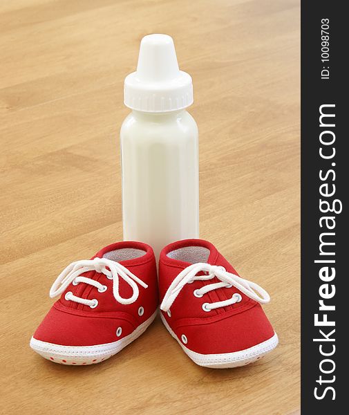 A baby bottle and a pair of shoes are sitting on a table. A baby bottle and a pair of shoes are sitting on a table.