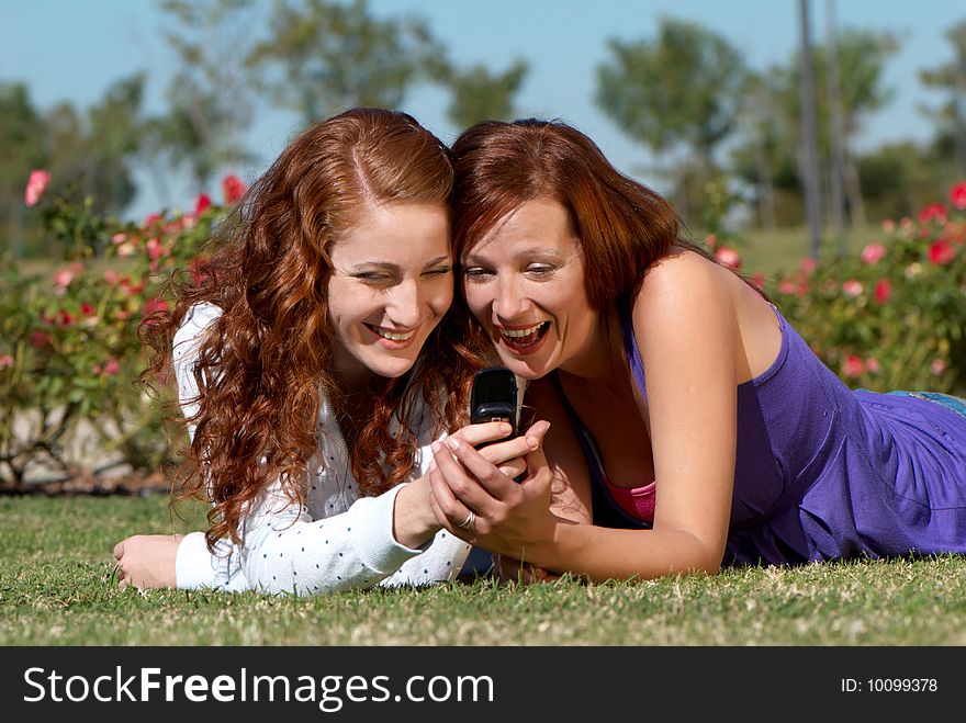 Two girlfriends with a mobile phone in park