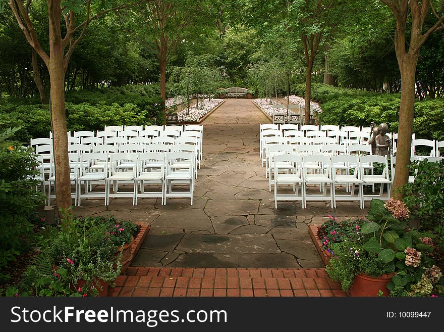 An outdoor sitting area is set up in a garden for a ceremony. An outdoor sitting area is set up in a garden for a ceremony.