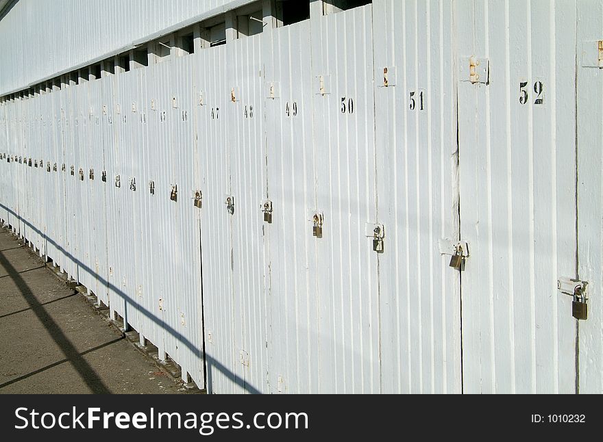 Detail of white, wooden building with a row of doors, each with a padlock. Detail of white, wooden building with a row of doors, each with a padlock