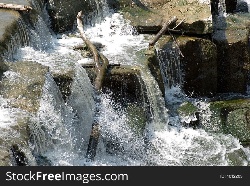A waterfall with several levels of rocks and a piece of wood sticking up out of water. Water frozen with fast shutter speed. A waterfall with several levels of rocks and a piece of wood sticking up out of water. Water frozen with fast shutter speed