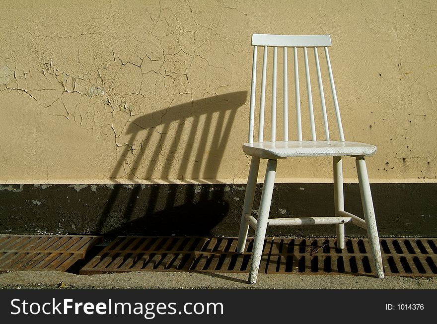White, wooden chair throwing a shadow on a yellow wall. White, wooden chair throwing a shadow on a yellow wall