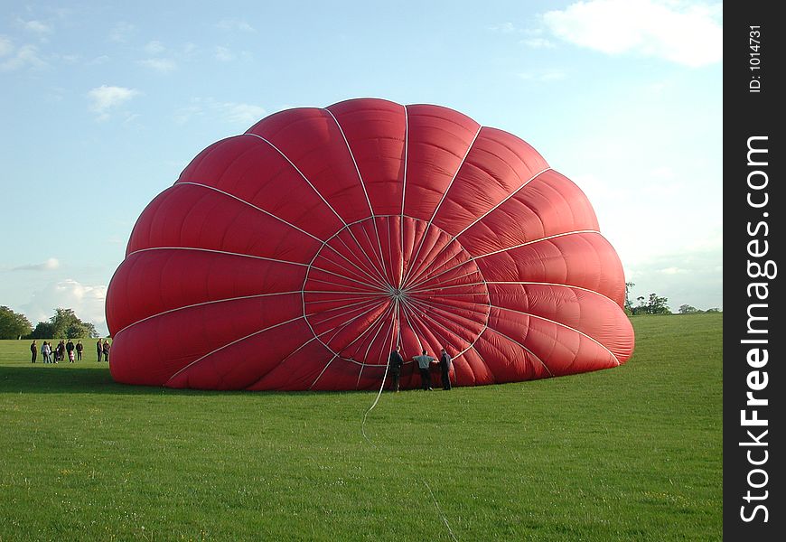 A colorful hot air balloon being inflated for launch, attented by tiny humans. A colorful hot air balloon being inflated for launch, attented by tiny humans...