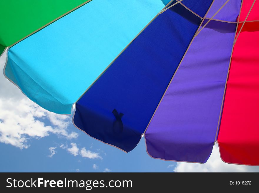 The Colorful Arc of a Beach Umbrella is Displayed against a Background of Blue Sky and Clouds. The Colorful Arc of a Beach Umbrella is Displayed against a Background of Blue Sky and Clouds.