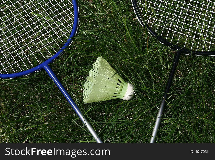 Two badminghton rackets laying in the grass with the ball in the middle. Two badminghton rackets laying in the grass with the ball in the middle