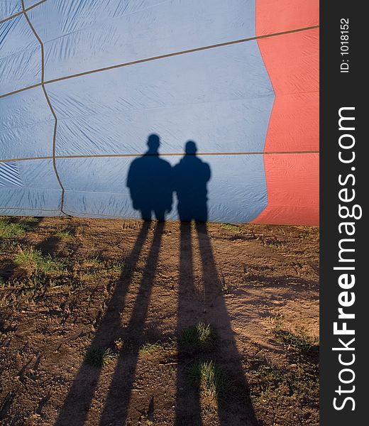 Long shadows of two men cast on a hot air balloon just before takeoff. Long shadows of two men cast on a hot air balloon just before takeoff