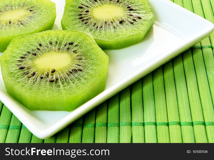 Sliced kiwi on white square plate on bamboo mat