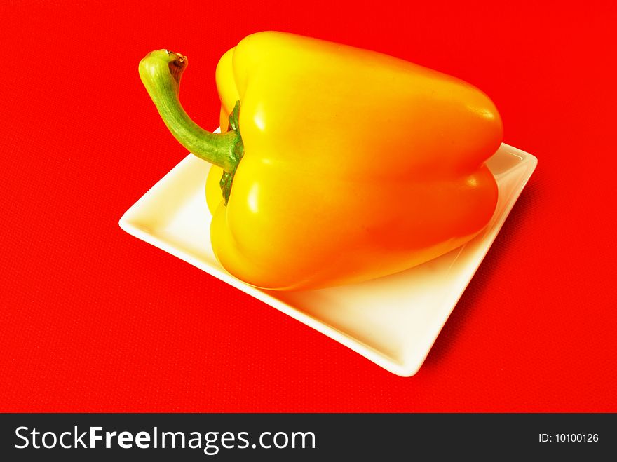 Yellow pepper on square white plate on red background