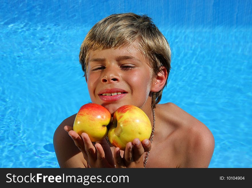 A 10 year old American - German boy sitting at a swimming pool in the summer sun and presenting delicious apples with almost closed eyes. A 10 year old American - German boy sitting at a swimming pool in the summer sun and presenting delicious apples with almost closed eyes