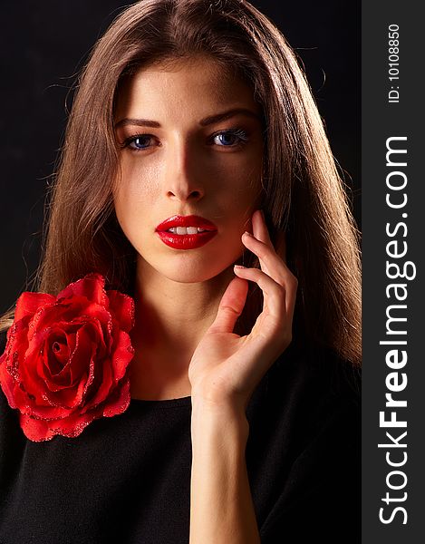 Portrait of a young beautiful brunettes with red lips in a black blouse decorated with a rose. Portrait of a young beautiful brunettes with red lips in a black blouse decorated with a rose