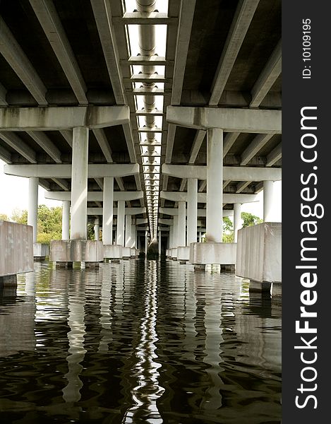 Underneath concrete bridge looking at supports and reflection in water