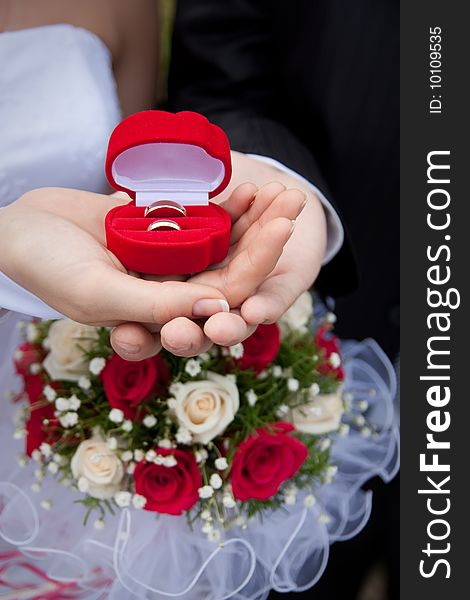Wedding rings in hands of a newly-married couple on a background of a bouquet