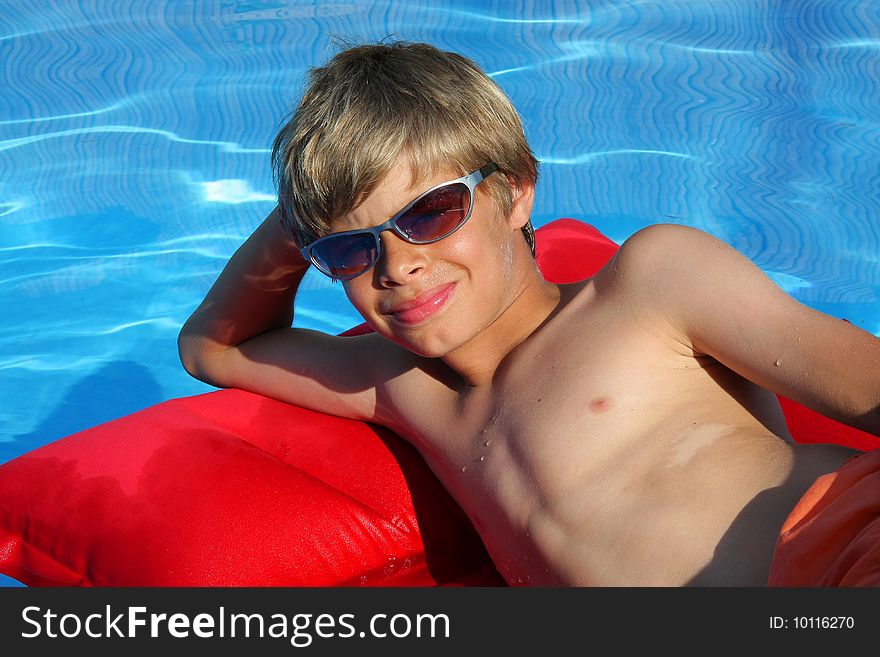 A 10 - year old American - German boy with sun glasses photographed in the summer sun while relaxing on an airbed. A 10 - year old American - German boy with sun glasses photographed in the summer sun while relaxing on an airbed