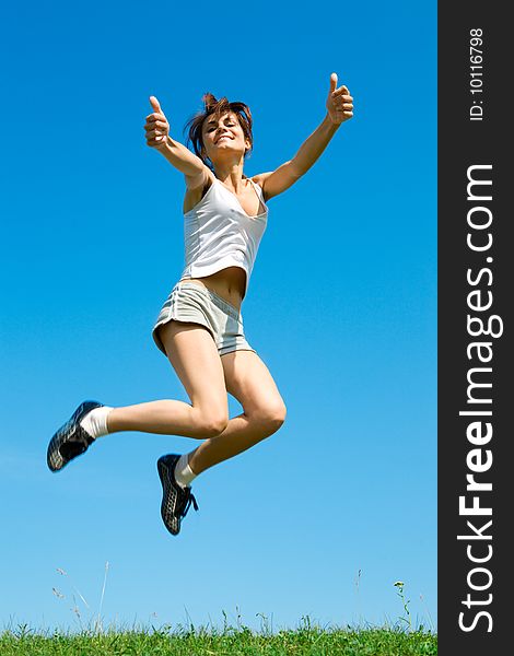 Happy young woman is jumping on green grass under sky