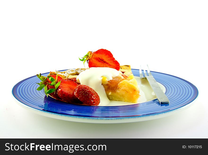 Slice of apple and strawberry pie with strawberries, cream and a fork on a blue plate with a white background. Slice of apple and strawberry pie with strawberries, cream and a fork on a blue plate with a white background