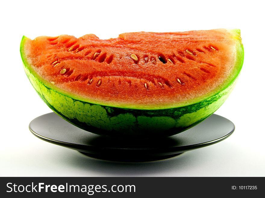 Slice of watermelon with green skin and red melon with seeds on a black plate with a white background. Slice of watermelon with green skin and red melon with seeds on a black plate with a white background