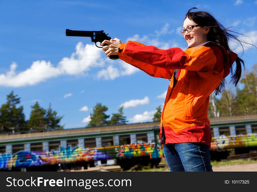 Young woman with long black hair holds a pistol and aims. Railway station. Young woman with long black hair holds a pistol and aims. Railway station.