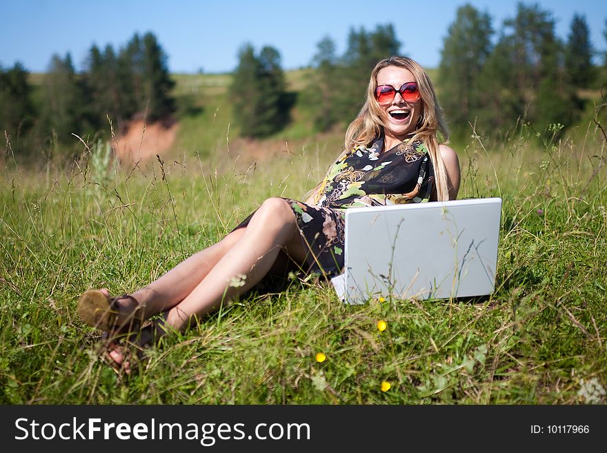 The girl sits at the laptop on the nature