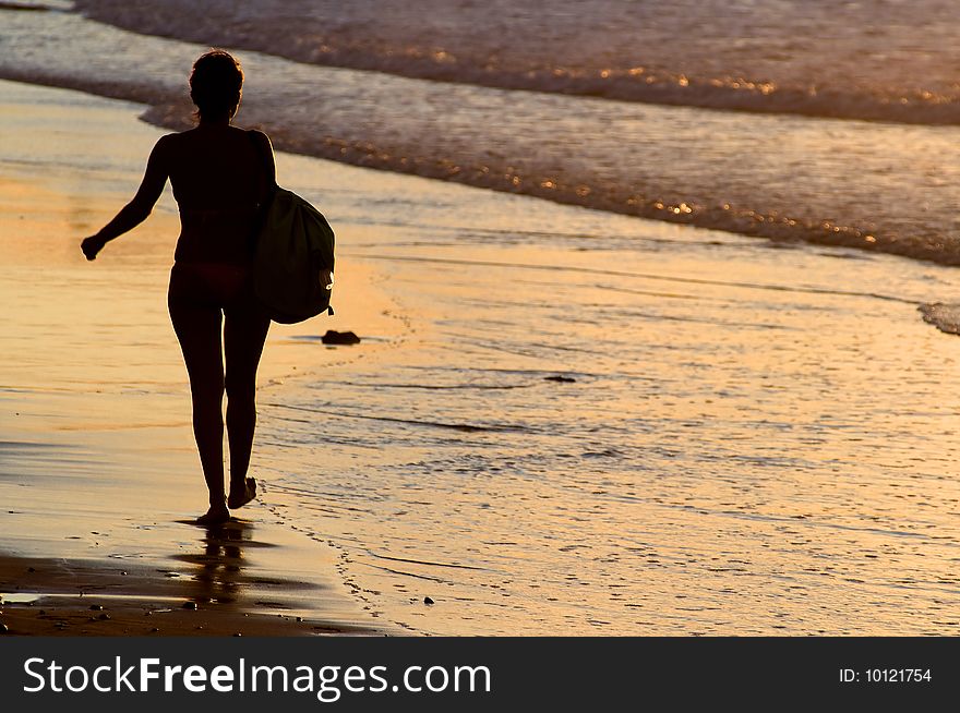Silhouette of woman walking by the seaside at sunset