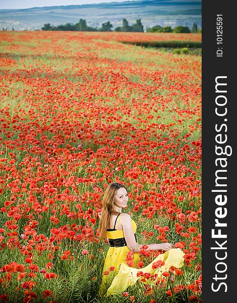 Beautiful young girl with yellow scarf in the poppy field, high angle view