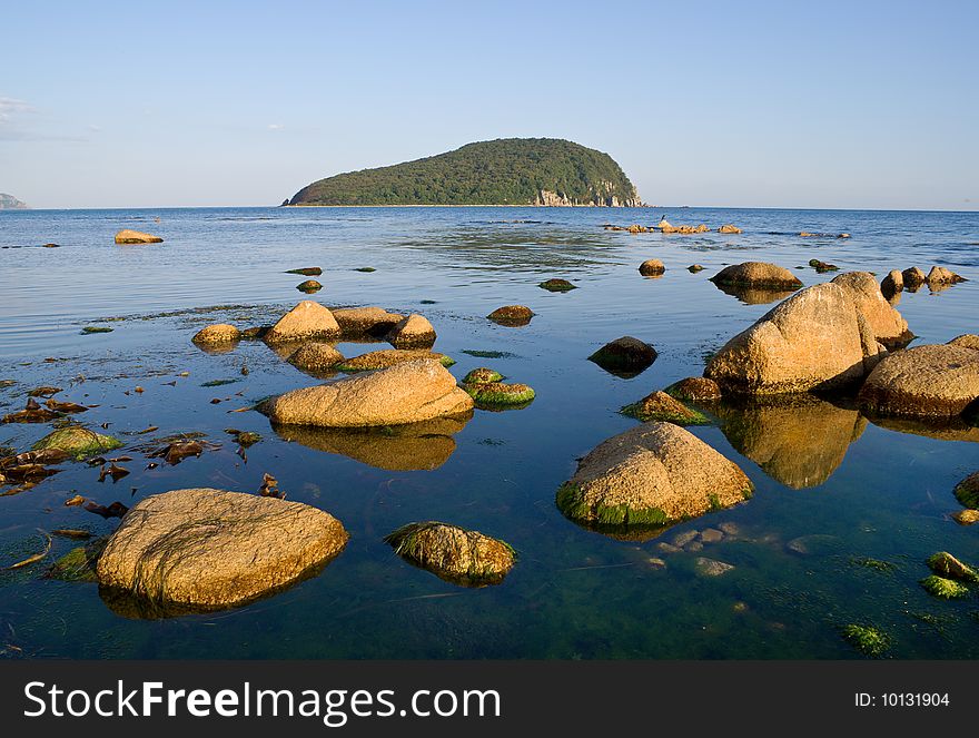 A ckose-uo of the stones in sea. On background is small green island. A ckose-uo of the stones in sea. On background is small green island.