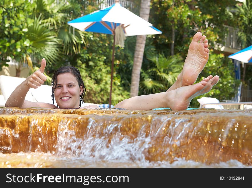 Young woman in a beautiful pool with palms in the background. She is showing a thumbs up sign. Young woman in a beautiful pool with palms in the background. She is showing a thumbs up sign.