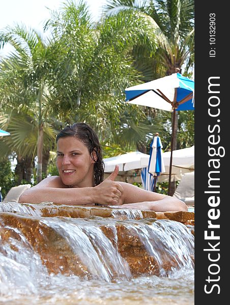 Young woman in a beautiful pool with palms in the background. She is showing a thumbs up sign. Young woman in a beautiful pool with palms in the background. She is showing a thumbs up sign.