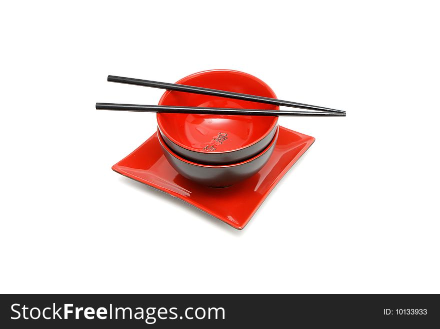 Black chopsticks on two red and black Japanese bowls and square plate isolated. Black chopsticks on two red and black Japanese bowls and square plate isolated