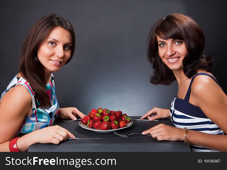 Plate with a strawberry on a table and two beautiful girls