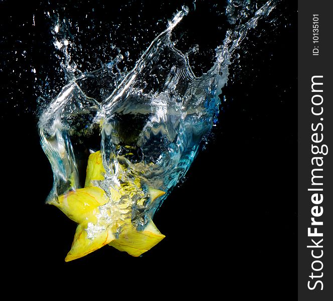 Starfruit tumbled into water, a lot of sparks and drops on black background, isolated