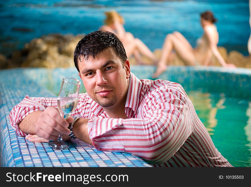 Portrait of a young man with a glass in the pool against the backdrop of two beautiful girls. Portrait of a young man with a glass in the pool against the backdrop of two beautiful girls