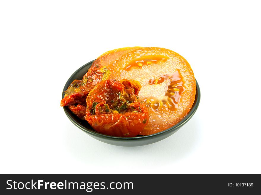 Sun dried tomatoes and slices of tomatoes in a small black bowl on a white background. Sun dried tomatoes and slices of tomatoes in a small black bowl on a white background
