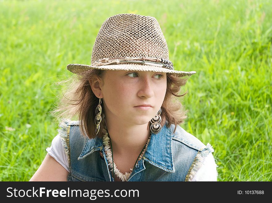 Portrait of a girl in the hat with blond hair and earrings on the background of grass. Portrait of a girl in the hat with blond hair and earrings on the background of grass