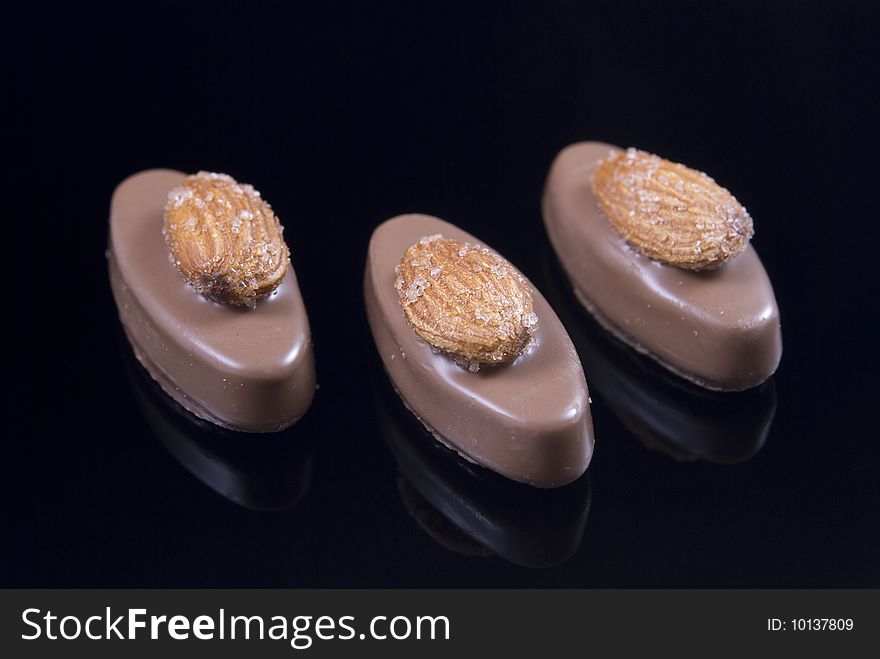 Three almond chocolate candies isolated on black background