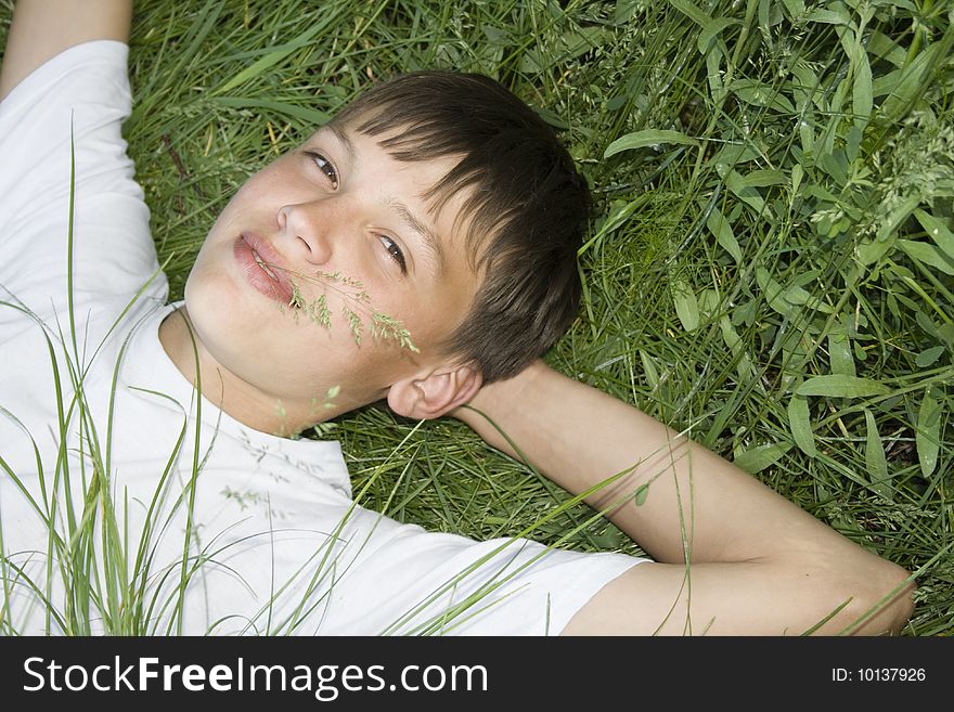 Dreamy teenager is relaxing, and he lies on the grass. Dreamy teenager is relaxing, and he lies on the grass