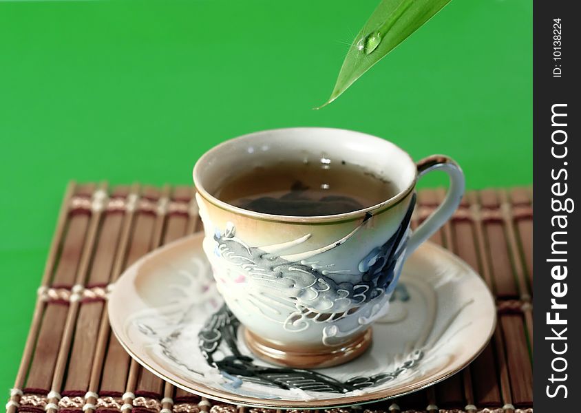 A cup of green tea and a drop of water on a green background